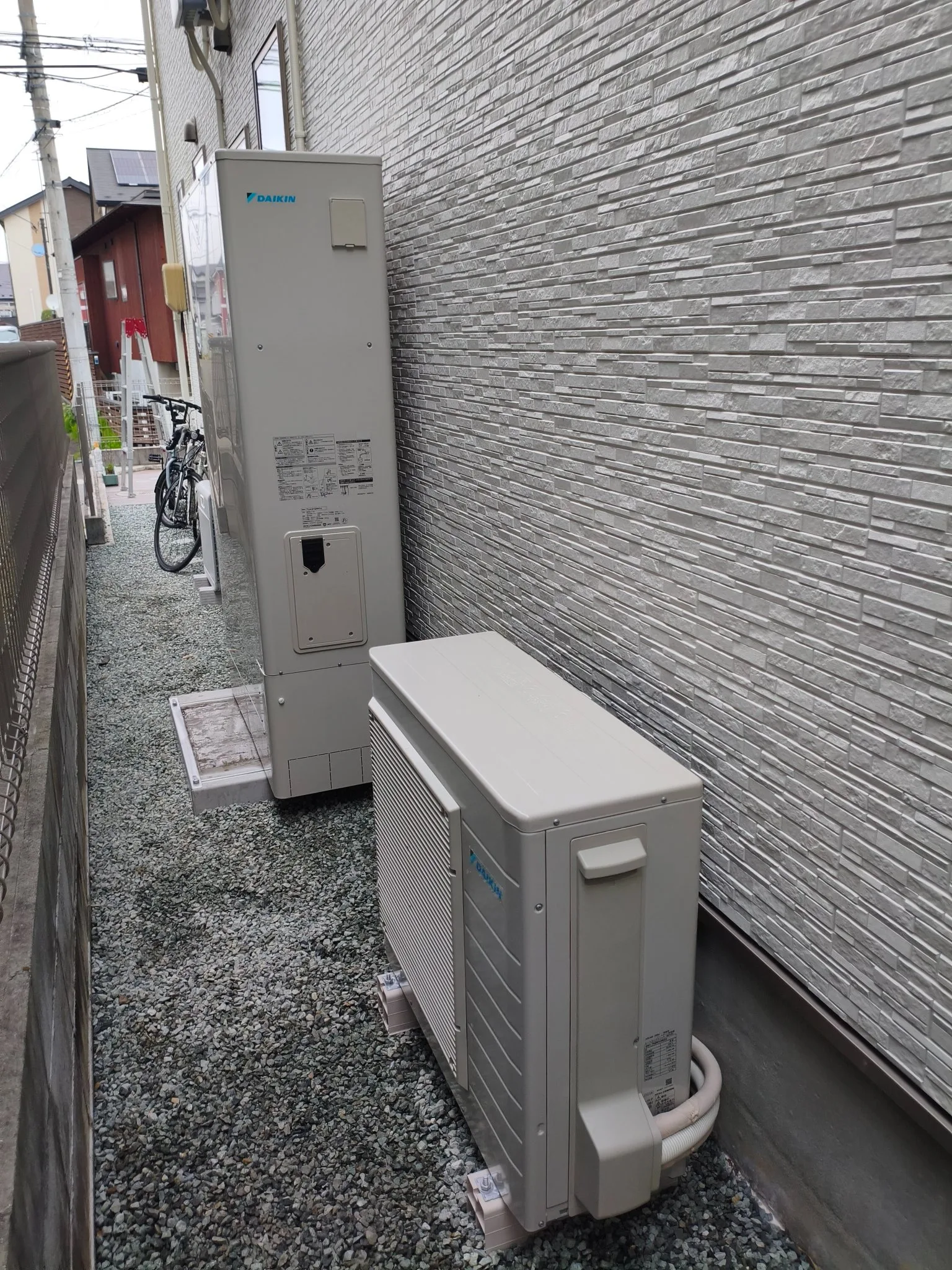 隣家が近い通路に設置されたエコキュートの貯湯タンクとヒートポンプ