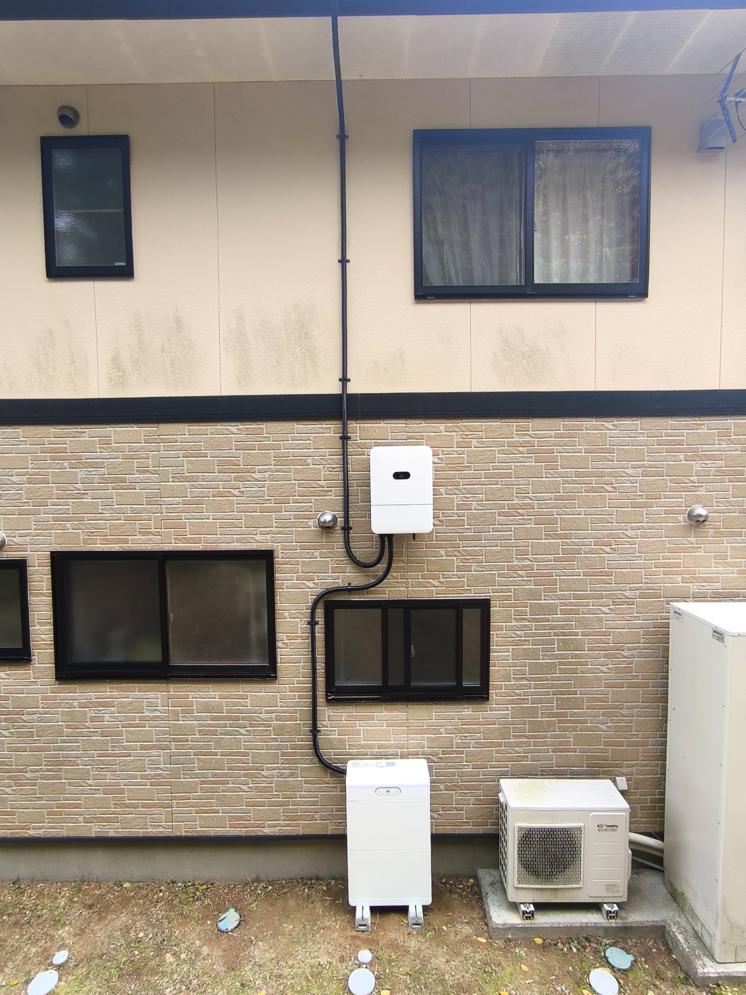 住宅の外壁に設置されたファーウェイのハイブリッドパワーコンディショナと、地面に据えた蓄電池ユニット