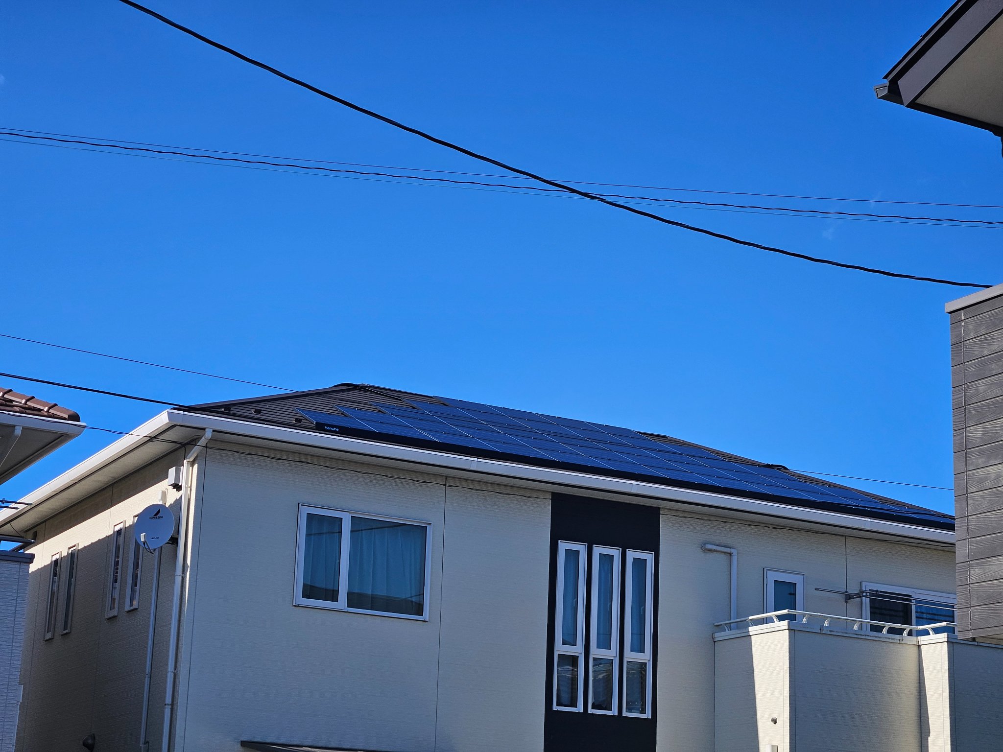 白い外壁の戸建て住宅の寄棟屋根に設置された黒い太陽光パネル