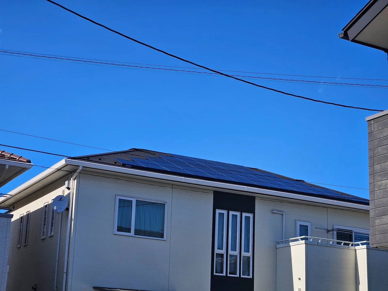 白い外壁の戸建て住宅の外観。寄棟屋根に黒い太陽光パネル