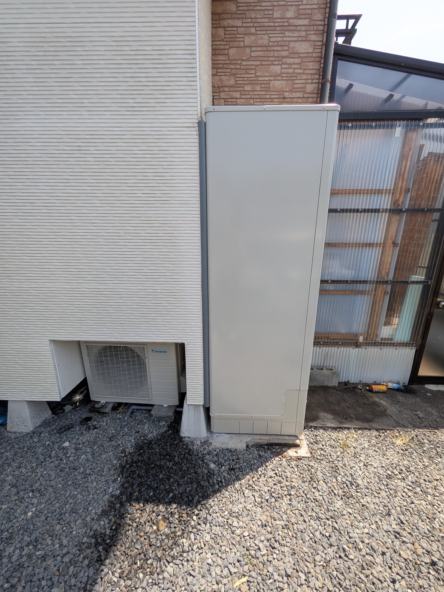 建物のすき間に設置された薄型の貯湯タンクと、奥のヒートポンプユニット