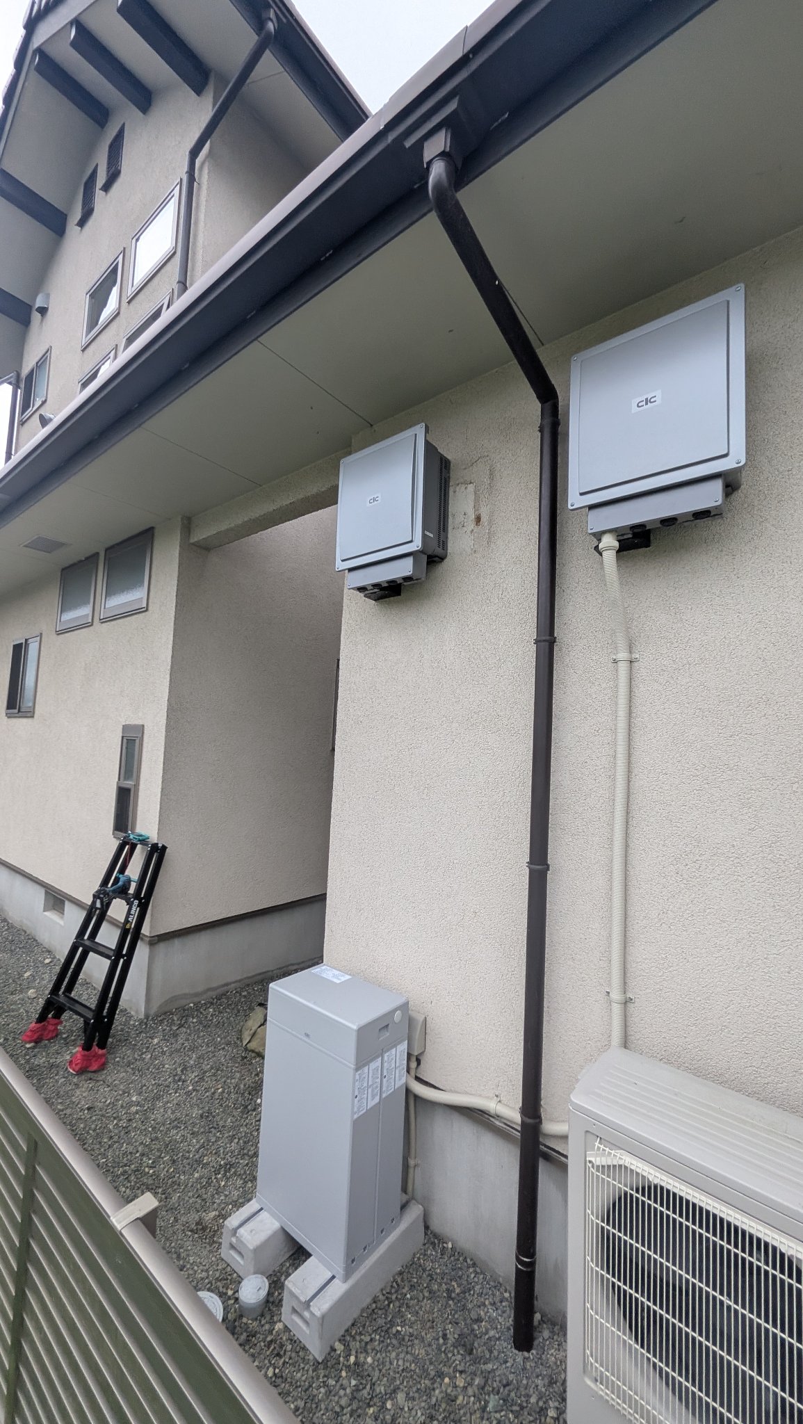 住宅の外壁に設置されたパワーコンディショナ2台と屋外の切替盤