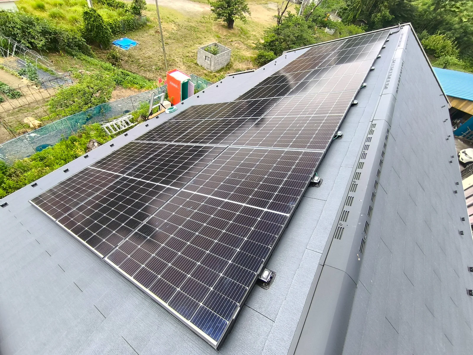 スレート屋根の片面に設置した太陽光パネルを俯瞰。山あいの住宅、棟換気が見える